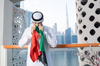 هوية اليوم الوطني الإماراتي 51، الإحتفال باليوم الوطني الإماراتي، يوم استقلال الإمارات، الاعتزاز والفخر بإنجازات البلاد، الحب والانتماء للوطن، رجل عربي خليجي إماراتي يرتدي الكندورة والغترة البيضاء يقوم بتقبيل علم الإمارات العربية المتحدة