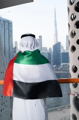 ايماءات الفخر و الإعجاب، الاحتفال بذكرى استقلال دولة الإمارات العربية المتحدة، اليوم الوطني الإماراتي 2 ديسمبر، صورة مقربة من الخلف لرجل عربي خليجي اماراتي يرتدي الكندورة و الغترة يضع علم الإمارات على كتفيه