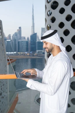 ايماءات السعادة والسرور، استخدام جهاز تقني حديث ومتطور، رجل عربي خليجي اماراتي يرتدي الكندورة والغترة البيضاء يستخدم الحاسوب المحمول، إنجاز مهام العمل عن بعد، إدارة شؤون الأعمال وتنظيمها عبر اللابتوب