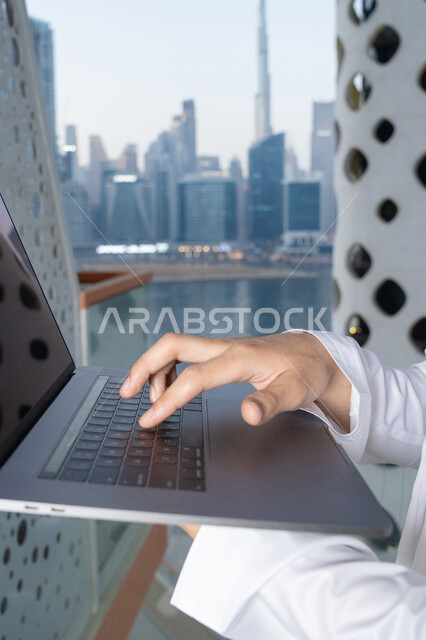 ايماءات السعادة والسرور، استخدام جهاز تقني حديث ومتطور، رجل عربي خليجي اماراتي يرتدي الكندورة والغترة البيضاء يستخدم الحاسوب المحمول، إنجاز مهام العمل عن بعد، إدارة شؤون الأعمال وتنظيمها عبر اللابتوب