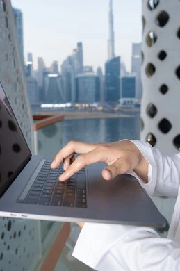 Gestures of happiness and pleasure, using a modern and advanced technical device, an Arab Gulf Emirati man wearing a white kandura and ghutra using a laptop, completing work tasks remotely, managing and organizing business affairs via the laptop