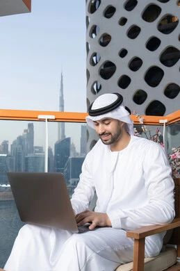 إدارة شؤون الأعمال وتنظيمها عبر اللابتوب، ايماءات السعادة والسرور، استخدام جهاز تقني حديث ومتطور، رجل عربي خليجي اماراتي يرتدي الكندورة والغترة البيضاء يستخدم الحاسوب المحمول، إنجاز مهام العمل عن بعد