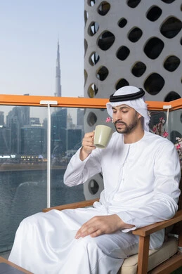Enjoying hot drinks, an Emirati Gulf Arab man wearing a white kandura and ghutra drinking coffee in a cafe, gestures of happiness and pleasure, spending free time sipping his favorite drink, eating warm winter herbs