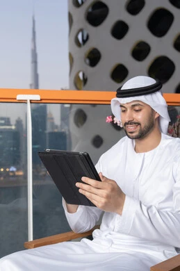 ايماءات السرور والسعادة، استخدام جهاز تقني حديث ومتطور، رجل عربي خليجي اماراتي يرتدي الكندورة والغترة البيضاء يستخدم الجهاز اللوحي، إنجاز مهام العمل عن بعد، إدارة شؤون الأعمال وتنظيمها عبر الايباد
