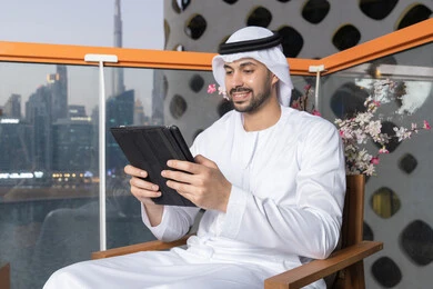 ايماءات السرور والسعادة، استخدام جهاز تقني حديث ومتطور، رجل عربي خليجي اماراتي يرتدي الكندورة والغترة البيضاء يستخدم الجهاز اللوحي، إنجاز مهام العمل عن بعد، إدارة شؤون الأعمال وتنظيمها عبر الايباد