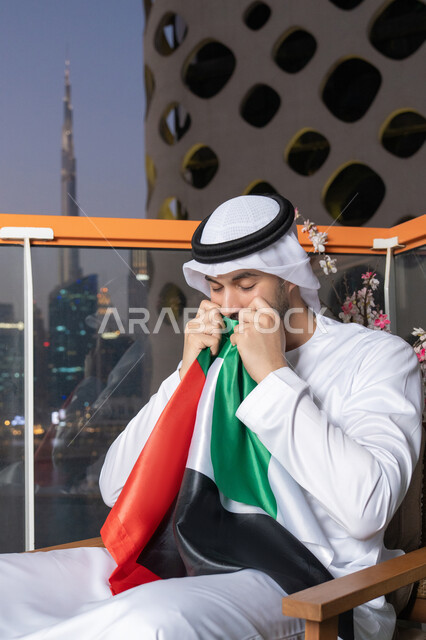 الإحتفال باليوم الوطني الإماراتي، هوية اليوم الوطني الإماراتي 51 ، يوم استقلال الإمارات، الاعتزاز والفخر بإنجازات البلاد، الحب والانتماء للوطن، رجل عربي خليجي إماراتي يرتدي الكندورة والغترة البيضاء يقوم بتقبيل علم الإمارات العربية المتحدة
