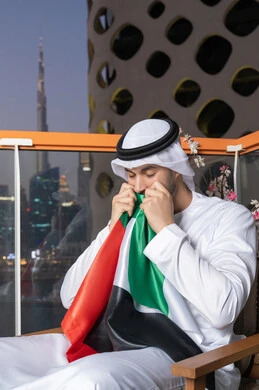 Celebrating UAE National Day, UAE National Day 51 identity, UAE Independence Day, pride in the country's achievements, love and belonging to the homeland, an Emirati Gulf Arab man wearing a white kandura and ghutra kissing the UAE flag