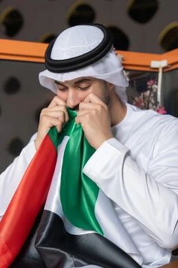 UAE National Day 51 identity, UAE National Day celebration, UAE Independence Day, pride in the country's achievements, love and belonging to the homeland, an Emirati Gulf Arab man wearing a white kandura and ghutra kissing the UAE flag