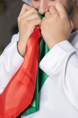 Celebrating UAE National Day, UAE National Day 51 identity, UAE Independence Day, pride in the country's achievements, love and belonging to the homeland, an Emirati Gulf Arab man wearing a white kandura and ghutra kissing the UAE flag