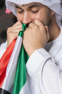 Celebrating UAE National Day, UAE National Day 51 identity, UAE Independence Day, pride in the country's achievements, love and belonging to the homeland, an Emirati Gulf Arab man wearing a white kandura and ghutra kissing the UAE flag