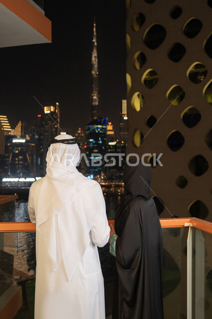 النظر الى الابراج وناطحات السحاب، النمو والتقدم العمراني للمنشآت في الامارات، مفهوم المحبة والالفة بين الزوجان، الاهتمام بالمظهر الخارجي، رجل عربي خليجي إماراتي يرتدي الكندورة والغترة البيضاء يقف مع زوجته