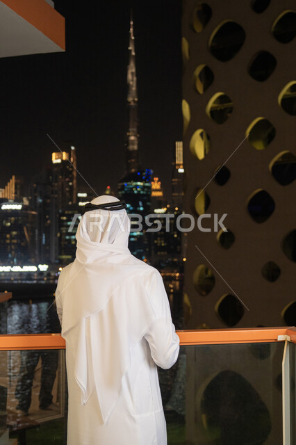 الاهتمام بالمظهر الخارجي، مفهوم الرجولة والأناقه، رجل عربي خليجي إماراتي يرتدي الكندورة والغترة البيضاء ينظر الى الابراج وناطحات السحاب، النمو والتقدم العمراني للمنشآت في الامارات