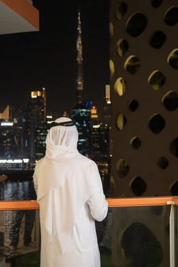 الاهتمام بالمظهر الخارجي، مفهوم الرجولة والأناقه، رجل عربي خليجي إماراتي يرتدي الكندورة والغترة البيضاء ينظر الى الابراج وناطحات السحاب، النمو والتقدم العمراني للمنشآت في الامارات