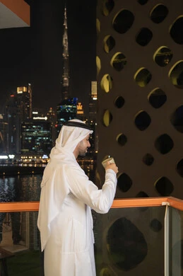 Spending free time sipping your favorite drink, eating warm winter herbs, enjoying hot drinks, an Emirati Gulf Arab man wearing a white kandura and ghutra drinking coffee in a cafe, gestures of happiness and pleasure