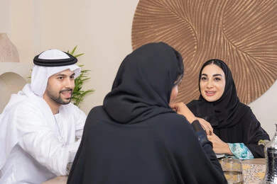 تعابير السعادة والسرور، جلسة وناسة بين الأصدقاء، شرب القهوة العربية، تبادل الأخبار والأحاديث، حسن إكرام الضيف، قضاء وقت عائلي ممتع، اجواء الأسرة السعيدة، عائلة عربية خليجية اماراتية يجلسون خلف الطاولة في المنزل، تناول القهوة العربية الساخنة