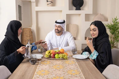 اجواء الأسرة السعيدة، شرب القهوة العربية، تبادل الأخبار والأحاديث، حسن إكرام الضيف، قضاء وقت عائلي ممتع، موسم الفاكهة الصحية اللذيذة، التفاهم والمحبة بين الزوجين، عائلة عربية خليجية اماراتية يجلسون خلف الطاولة في المنزل، تناول الفواكه الطازجة بإيماءات السعادة