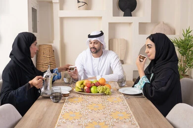 اجواء الأسرة السعيدة، شرب القهوة العربية، تبادل الأخبار والأحاديث، حسن إكرام الضيف، قضاء وقت عائلي ممتع، موسم الفاكهة الصحية اللذيذة، التفاهم والمحبة بين الزوجين، عائلة عربية خليجية اماراتية يجلسون خلف الطاولة في المنزل، تناول الفواكه الطازجة بإيماءات السعادة