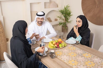 اجواء الأسرة السعيدة، شرب القهوة العربية، تبادل الأخبار والأحاديث، حسن إكرام الضيف، قضاء وقت عائلي ممتع، موسم الفاكهة الصحية اللذيذة، التفاهم والمحبة بين الزوجين، عائلة عربية خليجية اماراتية يجلسون خلف الطاولة في المنزل، تناول الفواكه الطازجة بإيماءات السعادة