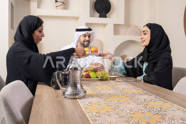 حسن إكرام الضيف، قضاء وقت عائلي ممتع، سناك خفيف ومنعش، موسم الفاكهة الصحية اللذيذة، التفاهم والمحبة بين الزوجين، اجواء الأسرة السعيدة، عائلةة عربية خليجية اماراتية يجلسون خلف الطاولة في المنزل يقومان بتناول الفواكه الطازجة بإيماءات السعادة والسرور
