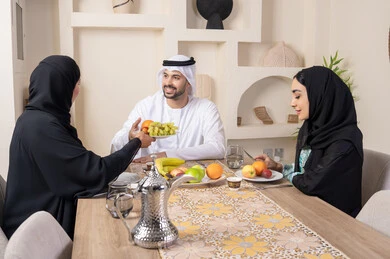 حسن إكرام الضيف، قضاء وقت عائلي ممتع، سناك خفيف ومنعش، موسم الفاكهة الصحية اللذيذة، التفاهم والمحبة بين الزوجين، اجواء الأسرة السعيدة، عائلةة عربية خليجية اماراتية يجلسون خلف الطاولة في المنزل يقومان بتناول الفواكه الطازجة بإيماءات السعادة والسرور
