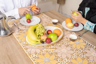 قضاء وقت عائلي ممتع، سناك خفيف ومنعش، موسم الفاكهة الصحية اللذيذة، التفاهم والمحبة بين الزوجين، اجواء الأسرة السعيدة، زوجان عربيان خليجيان اماراتيان يجلسان خلف الطاولة في المنزل يقومان بتناول الفواكه الطازجة بإيماءات السعادة والسرور