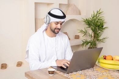 ارتداء سماعات الاذن، اداء مهام العمل عن بعد، رجل عربي خليجي إماراتي يرتدي الكندورة والغترة يجلس على طاولة في المنزل يعمل على الحاسب المحمول، تناول وجبة فطور صحية، أنواع الفاكهة الطازجة والقهوة العربية التقليدية، دمج التكنولوجيا الحديثة مع الروتين اليومي ارتداء سماعات الاذن، اداء مهام العمل عن بعد، رجل عربي خليجي إماراتي يرتدي الكندورة والغترة يجلس على طاولة في المنزل يعمل على الحاسب المحمول، تناول وجبة فطور صحية، أنواع الفاكهة الطازجة والقهوة العربية التقليدية، دمج التكنولوجيا الحديثة مع الروتين اليومي