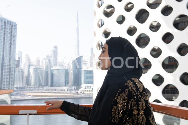 منظر جوي لناطحات السحاب, الهدوء والاستمتاع بالنظر من شرفة راقية, قضاء وقت ممتع في المقهى, شابة عربية خليجية اماراتية محجبة ترتدي عباءة سوداء مطرزة باللون الذهبي