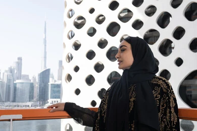 الهدوء والاستمتاع بالنظر من شرفة راقية, قضاء وقت ممتع في المقهى, شابة عربية خليجية اماراتية محجبة ترتدي عباءة سوداء مطرزة باللون الذهبي