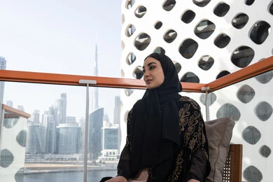 جلسة وناسة واستمتاع, لحظة صفاء راقية, شابة عربية خليجية اماراتية محجبة ترتدي عباءة سوداء مطرزة باللون الذهبي و تنظر من الشرفة, تصميم مقهى عصري