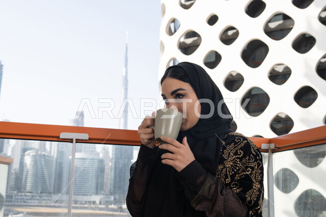الإستمتاع بشرب قهوة الصباح, قضاء وقت ممتع في المقهى, شابة عربية خليجية اماراتية محجبة ترتدي عباءة سوداء مطرزة باللون الذهبي