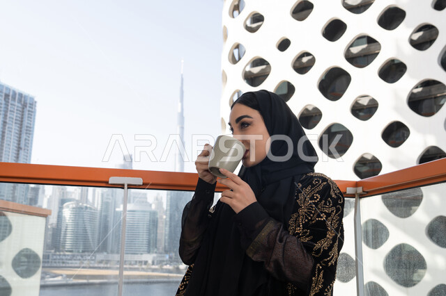 لحظة استرخاء راقية, قضاء وقت ممتع في المقهى, شابة عربية خليجية اماراتية محجبة ترتدي عباءة سوداء مطرزة باللون الذهبي و تشرب كوب من المشروب الدافئ