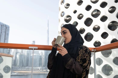 لحظة استرخاء راقية, قضاء وقت ممتع في المقهى, شابة عربية خليجية اماراتية محجبة ترتدي عباءة سوداء مطرزة باللون الذهبي و تشرب كوب من المشروب الدافئ
