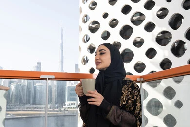 تأمل المشهد من بعيد, الهدوء والاستمتاع بالنظر من شرفة راقية, شابة عربية خليجية اماراتية محجبة ترتدي عباءة سوداء مطرزة باللون الذهبي, الاستمتاع بمشروب دافئ