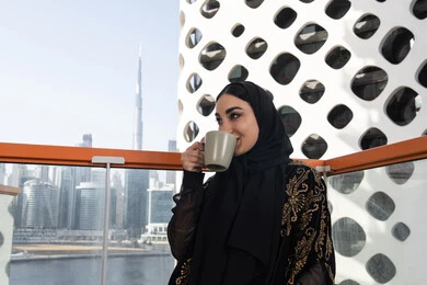 جلسة استرخاء مع فنجان قهوة, قضاء وقت ممتع في المقهى, شابة عربية خليجية اماراتية محجبة ترتدي عباءة سوداء مطرزة باللون الذهبي