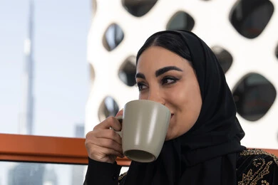 صورة مقربة لشابة عربية خليجية اماراتية محجبة ترتدي عباءة سوداء مطرزة باللون الذهبي, إيماءات سعادة و سرور, الاستمتاع بمشروب دافئ