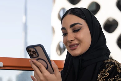 إيماءات الفرح والسرور لسماع الاخبار المفرحة، صورة مقربة لشابة عربية خليجية اماراتية محجبة مبتسمة ترتدي عباءة سوداء مطرزة باللون الذهبي, جلسة عصرية في مقهى حديث