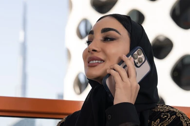 تعابير الاندماج والتركيز بالتحدث عبر الهاتف المحمول، قضاء اوقات ممتعة بتبادل الاخبار والأحاديث،  شابة عربية خليجية اماراتية محجبة مبتسمة ترتدي عباءة سوداء مطرزة باللون الذهبي