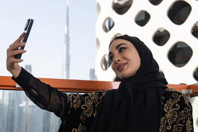 إلتقاط صور سيلفي تذكارية  بإستخدام الهاتف المحمول، إستخدام اجهزة تقنية حديثة، شابة عربية خليجية اماراتية محجبة مبتسمة ترتدي عباءة سوداء مطرزة باللون الذهبي