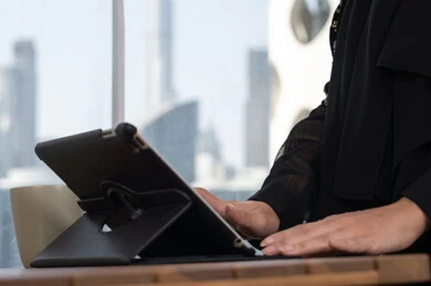 Close-up of a woman's hand professionally operating her tablet in a modern work environment, an Arab Gulf Emirati woman wearing a black abaya, completing work remotely