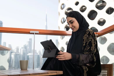 جلسة عمل هادئة مع إطلالة حضرية, احتراف الوظائف التقنية وتكنولوجيا المعلومات، متابعة آخر الأخبار على مواقع الانترنت، شابة عربية خليجية اماراتية محجبة ترتدي عباءة سوداء مطرزة باللون الذهبي
