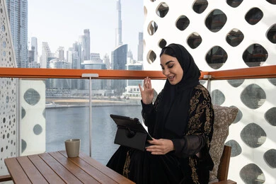 Taking advantage of modern technology and advanced technology, making video calls using a tablet, a veiled young Arab Gulf Emirati woman wearing a black abaya embroidered in gold, expressions of greeting and peace