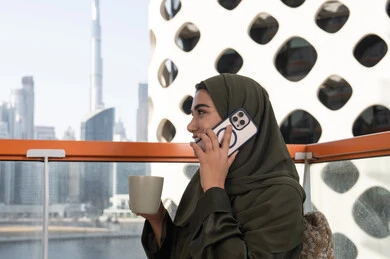 Chatting and talking with friends, enjoying a hot drink, a veiled Emirati Gulf Arab woman wearing a green abaya making a phone call in an outdoor cafe