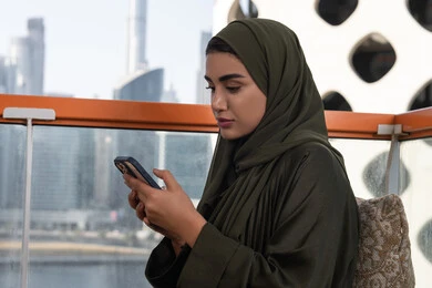 الاستمتاع بقضاء وقت ممتع في إحدى المقاهي الفارهة, تصفح وسائل التواصل الاجتماعي عبر الجوال, سيدة عربية خليجية اماراتية ترتدي الحجاب مع عباءة خضراء, استخدام التقنيات الحديثة والمتطورة
