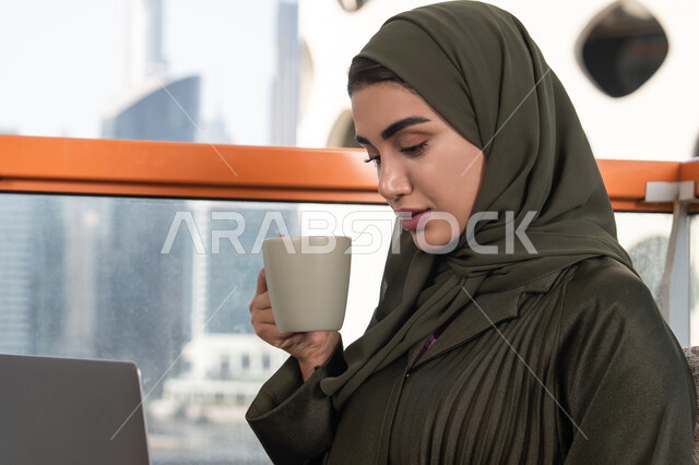 ايماءات التركيز و الاندماج, شابة عربية خليجية اماراتية محجبة ترتدي عباءة و حجاب, العمل عن بعد عن طريق الانترنت,الاستمتاع بالمشروب الساخن