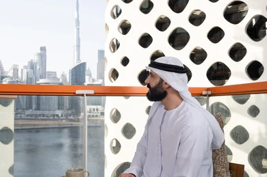 Entertainment and leisure during the holiday, a side view of an Emirati Gulf Arab man wearing a kandura and a white ghutrah sitting in a café contemplating the natural scenery, enjoying spending free time outdoors.