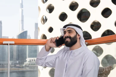 قضاء وقت ممتع فى الخارج , اجراء مكالمه هاتفيه، صورة مقربة لشاب عربي خليجي إماراتي يرتدي الكندورة والغترة البيضاء يجلس في المقهى ، مفهوم التكنولوجيا وإستخدام تقنيات حديثة, التواصل عن بعد, اجراء بث مباشر,التواصل مع الاهل والاصدقاء