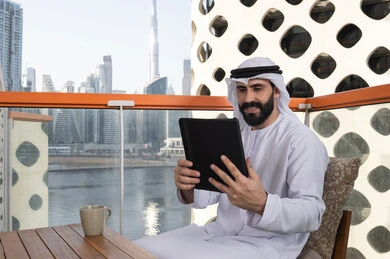 الاستمتاع بتناول المشروبات, استعمال التكنولوجيا والتقنيات الحديثة، الدردشة مع الأهل والأصدقاء، رجل عربي خليجي اماراتي يرتدي الكندورة و الغترة البيضاء يحمل بيده جهاز التابلت، تصفح مواقع التواصل الاجتماعي، استخدام تطبيقات وبرامج الأجهزة اللوحية