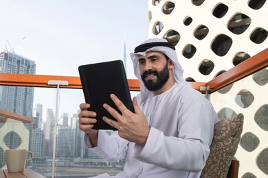عقد إجتماع عمل عبر الإنترنت, استعمال التكنولوجيا والتقنيات الحديثة، الدردشة مع الأهل والأصدقاء، رجل عربي خليجي اماراتي يرتدي الكندورة و الغترة البيضاء يحمل بيده جهاز التابلت، تصفح مواقع التواصل الاجتماعي، استخدام تطبيقات وبرامج الأجهزة اللوحية