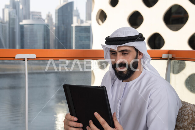 استعمال التكنولوجيا والتقنيات الحديثة، الدردشة مع الأهل والأصدقاء، صورة مقربة لرجل عربي خليجي اماراتي يرتدي الكندورة و الغترة البيضاء يحمل بيده جهاز التابلت، تصفح مواقع التواصل الاجتماعي، استخدام تطبيقات وبرامج الأجهزة اللوحية