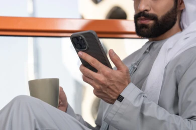 رجل عربي خليجي اماراتي يرتدي الكندورة والغترة البيضاء يمسك بيده الهاتف المحمول, تبادل الأحاديث والتواصل والأخبار مع الأهل والأصدقاء، استخدام جهاز تقني حديث ومتطور، العمل عن بعد، تصفح التطبيقات وبرامج التواصل الاجتماعي, تناول المشروب المفضل